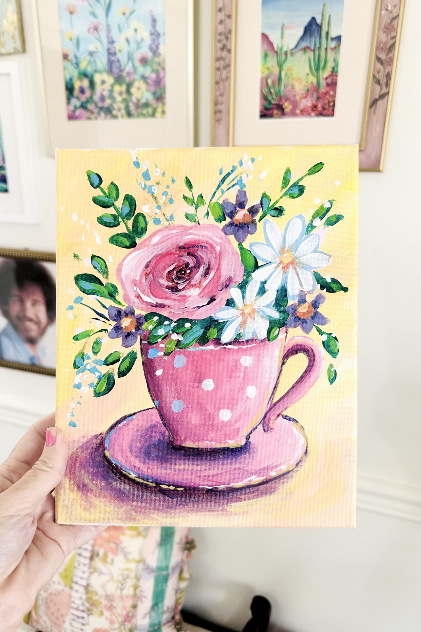 Finished painting of a pink and white polka dot tea cup with a large bouquet of wildflowers on a soft yellow background.